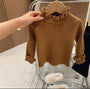 Brauner Rollkragenpullover für Kinder, gerippt, aus Wolle, auf Kleiderbügel, Hand hält Pullover.