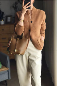 Frau in brauner Strickjacke und beiger Hose mit brauner Ledertasche, modisch, elegant.