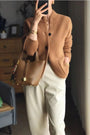 Frau in brauner Strickjacke und beiger Hose mit brauner Ledertasche, modisch, elegant.