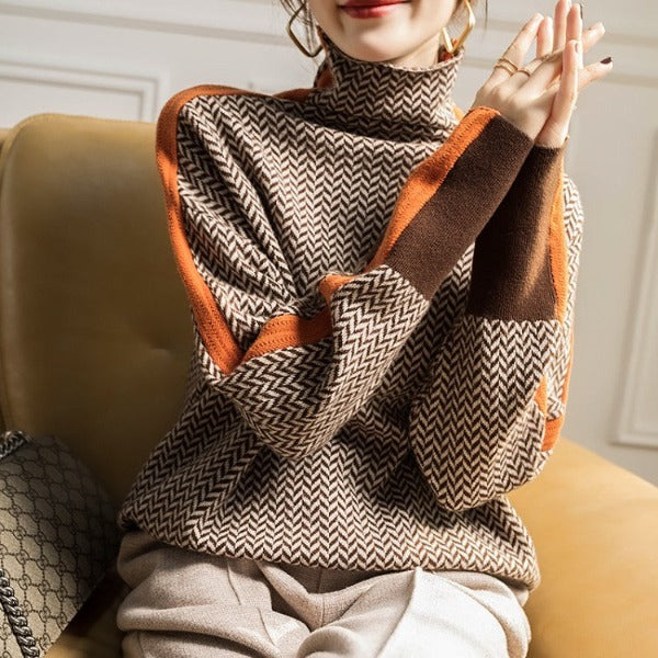 Frau in braunem Strickpullover mit Zickzackmuster und orangefarbenen Akzenten, sitzt auf Sofa.