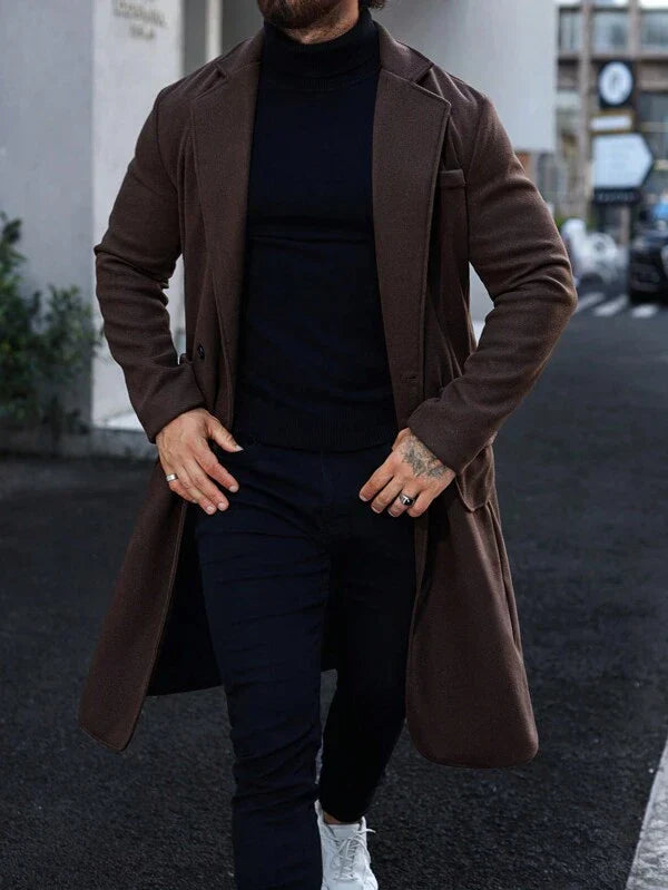 Mann in braunem Wollmantel, schwarzem Rollkragenpullover, dunkler Hose, weißen Sneakers.