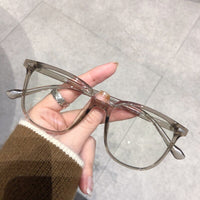 Transparente Brille, rechteckig, Kunststoff, modisch, unisex, Hand hält Brille, Nahaufnahme.