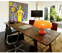 Moderner Konferenzraum mit Holztisch, orangefarbener Lampe, Kunstwerk und Flachbildschirm.