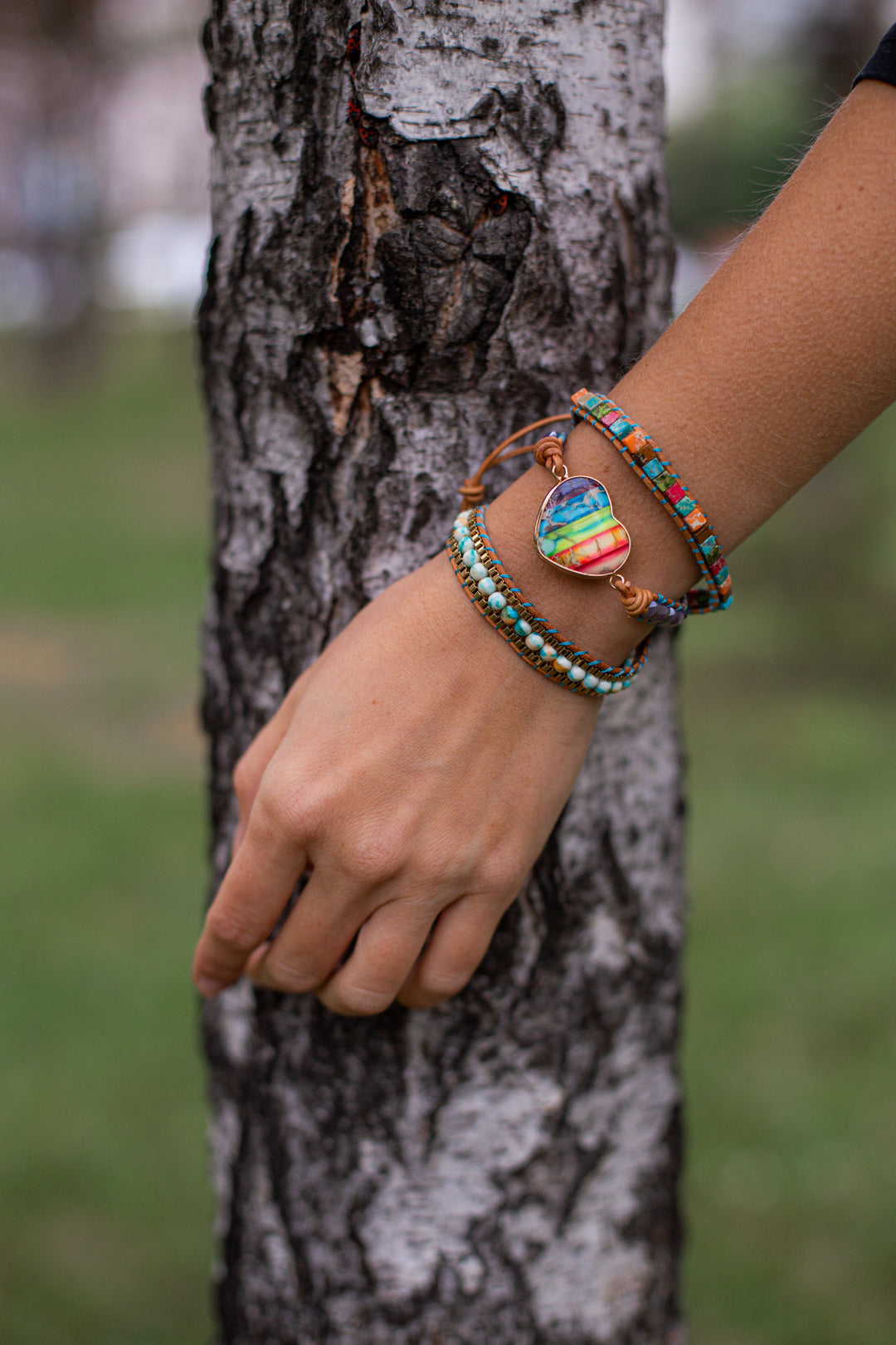 Frau mit bunten Armbändern aus Perlen und Herzanhänger vor Baumstamm im Freien.