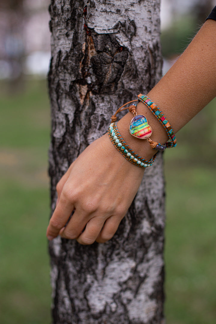 Frau mit bunten Armbändern aus Perlen und Herzanhänger vor Baumstamm im Freien.