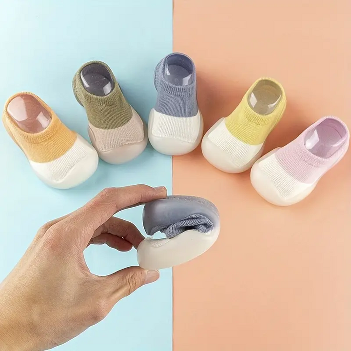 Fünf Paar bunte Babysocken mit rutschfester Sohle, weiches Material, auf zweifarbigem Hintergrund.