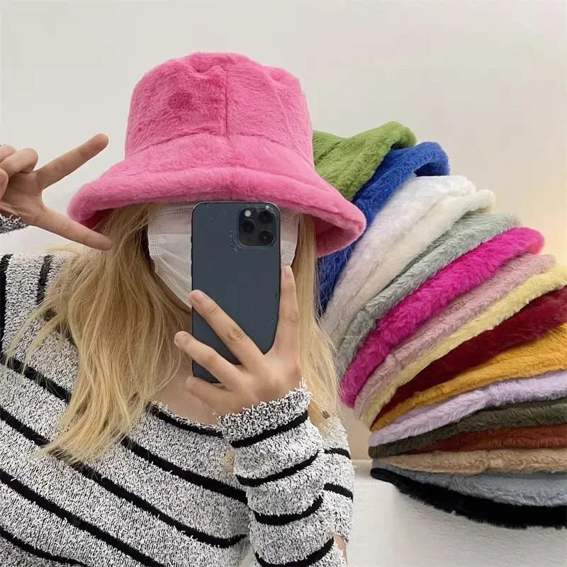 Frau mit rosa Plüschhut, gestreiftem Pullover, Smartphone, bunte Hüte im Hintergrund.