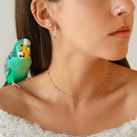 Frau mit Wellensittich, bunte Halskette, Ohrringe, weißes Spitzenkleid, Nahaufnahme.