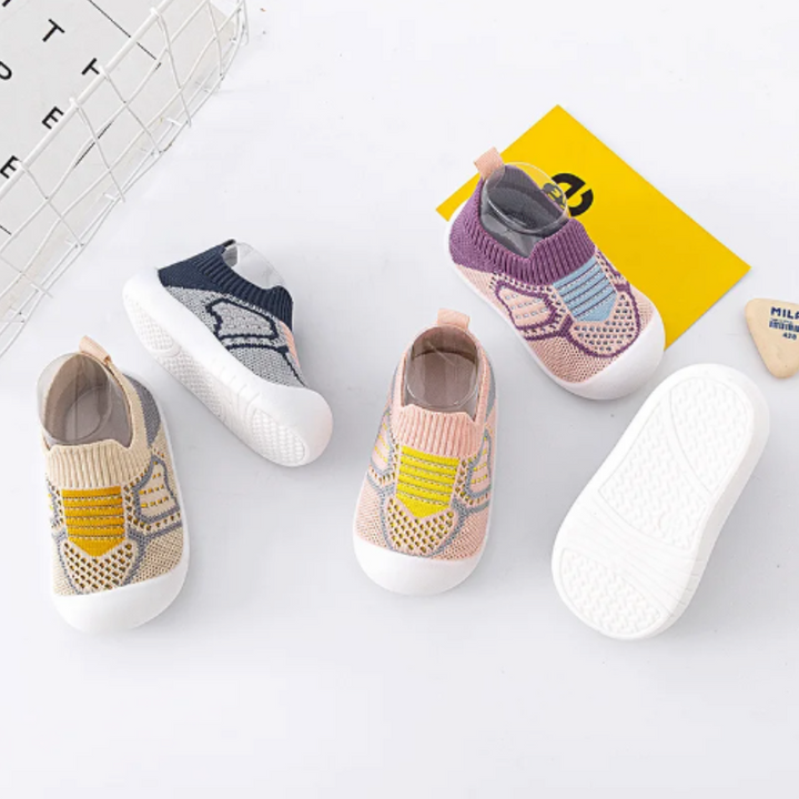 Vier Paar bunte Baby-Sneaker aus Strickstoff mit rutschfester Sohle auf weißem Hintergrund.