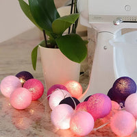 Bunte Lichterkette mit rosa und lila Kugeln auf Küchentheke neben weißem Mixer und Pflanze.