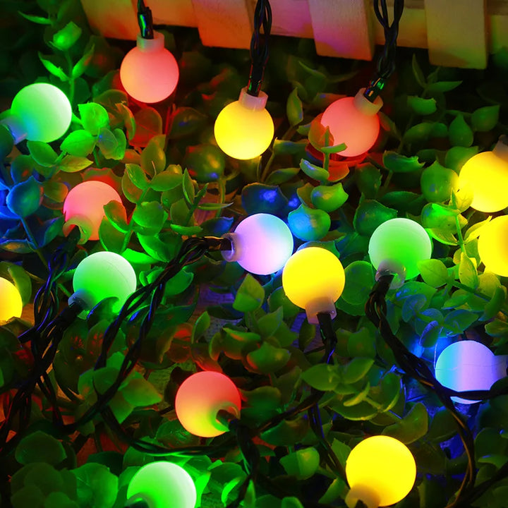 Bunte LED-Lichterkette auf grünen Blättern, dekorative Beleuchtung für Garten oder Party.