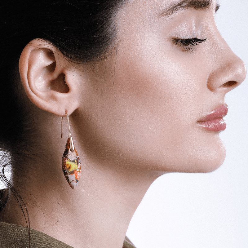 Frau mit buntem Ohrring, Tropfenform, handgefertigt, modisches Accessoire, Nahaufnahme.