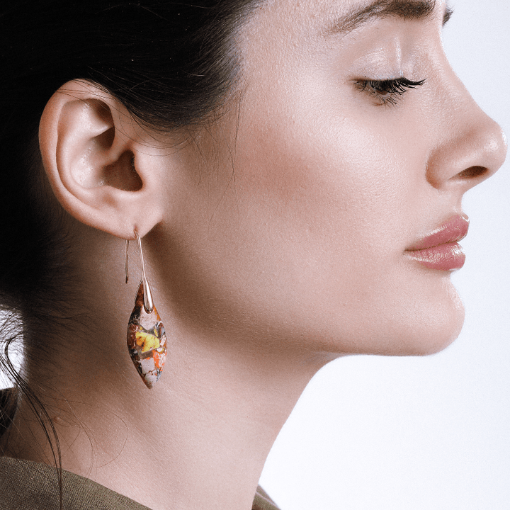 Frau mit buntem Ohrring, Tropfenform, handgefertigt, modisches Accessoire, Nahaufnahme.