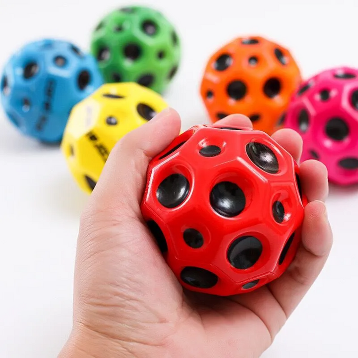 Roter Hundespielzeugball mit Löchern, Hand hält Ball, bunte Bälle im Hintergrund.