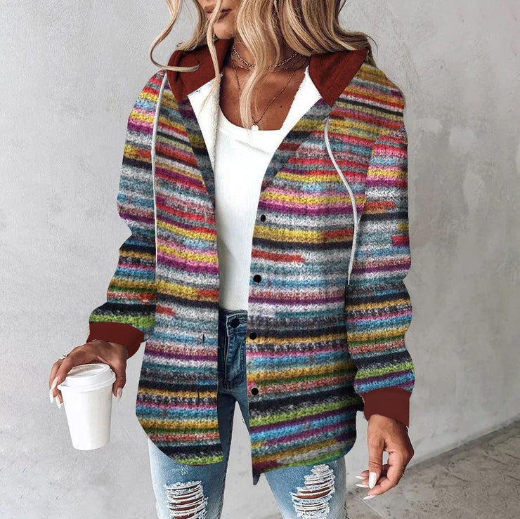 Frau in bunter gestreifter Strickjacke, weißem Top, zerrissenen Jeans, hält Kaffeebecher.