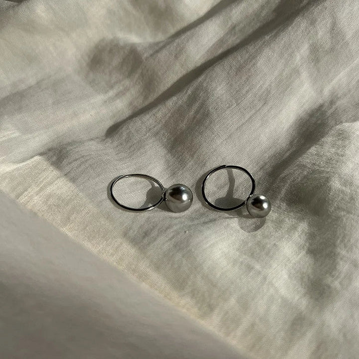 Silberne Perlenohrringe auf weißem Stoff, eleganter Schmuck, minimalistisches Design.