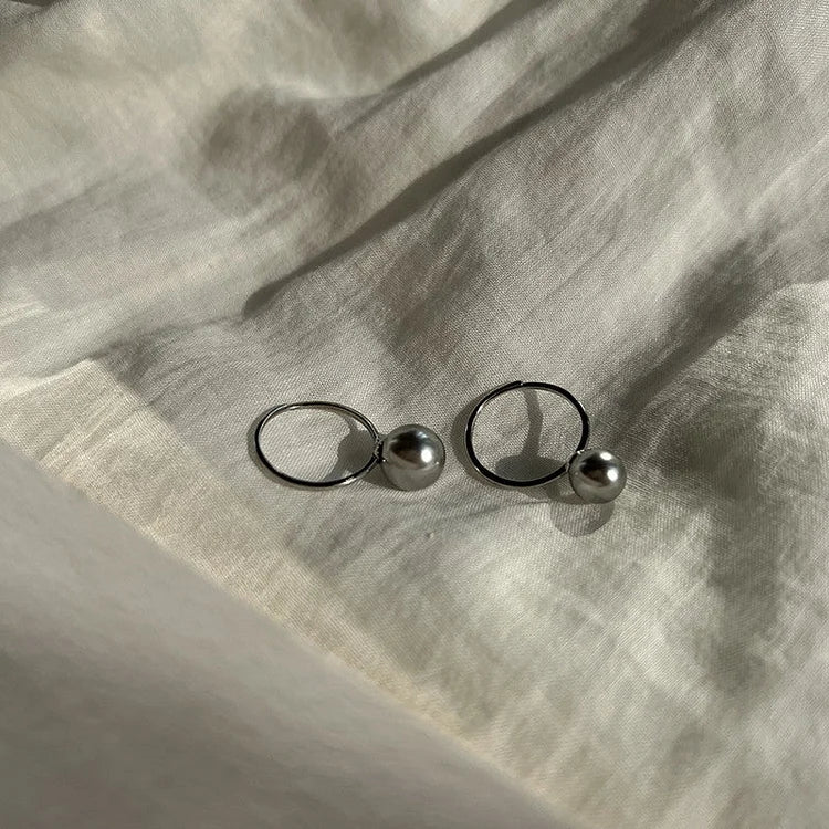 Silberne Perlenohrringe auf weißem Stoff, eleganter Schmuck, minimalistisches Design.