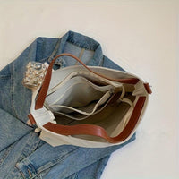 Beigefarbene Canvas-Schultertasche mit braunen Ledergriffen auf blauer Jeansjacke.
