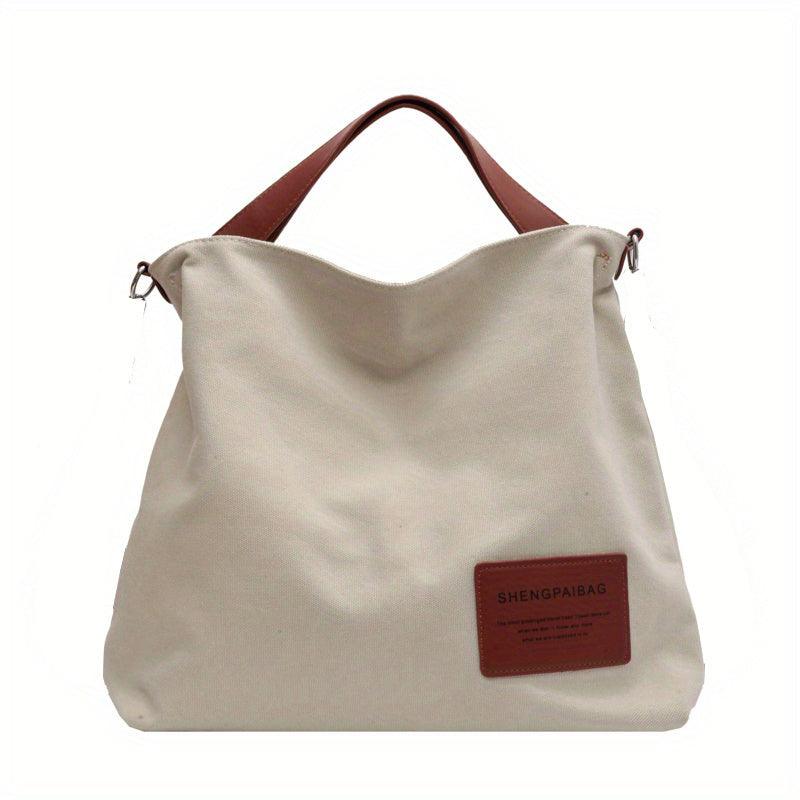 Beige Canvas-Schultertasche mit braunen Griffen und Lederetikett, modisch und geräumig.