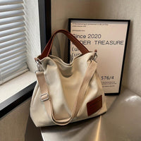 Beige Canvas-Schultertasche mit braunen Ledergriffen auf Tisch, modisch und praktisch.