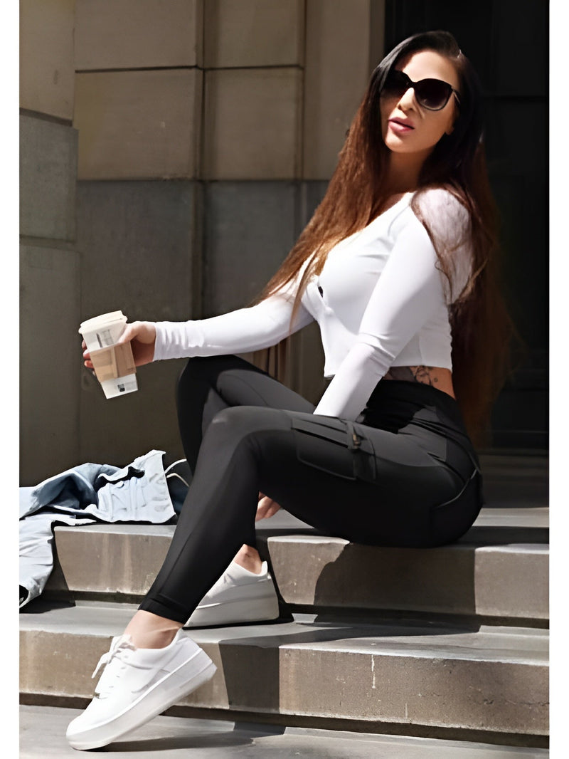 Frau in schwarzer Cargo-Leggings, weißem Oberteil, Sonnenbrille, hält Kaffee, sitzt auf Treppe.