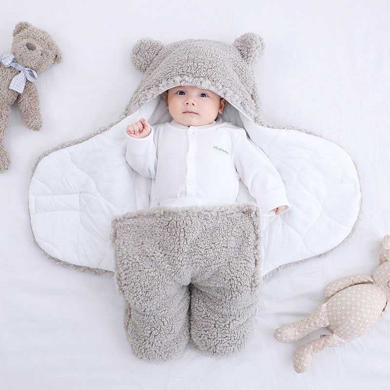 Baby in grauem Teddy-Fleece-Fußsack mit Kapuze, weich und warm, auf weißem Hintergrund.