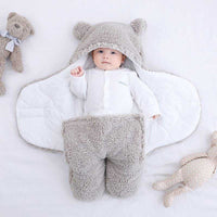 Baby in grauem Teddy-Fleece-Fußsack mit Kapuze, weich und warm, auf weißem Hintergrund.
