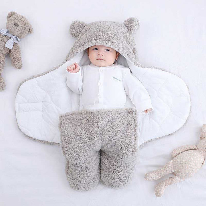 Baby in grauem Teddy-Fleece-Fußsack mit Kapuze, weich und warm, auf weißem Hintergrund.