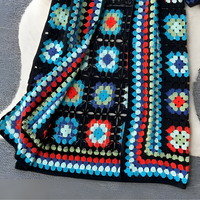 Bunte gehäkelte Decke mit geometrischen Mustern auf grauem Hintergrund.