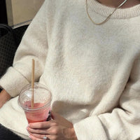 Frau in cremefarbenem Pullover hält Erdbeer-Smoothie im Plastikbecher mit Strohhalm.