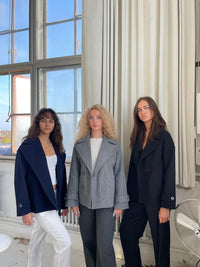 Drei Frauen in eleganten Blazern vor einem Fenster, modische Damenbekleidung, Herbstmode.