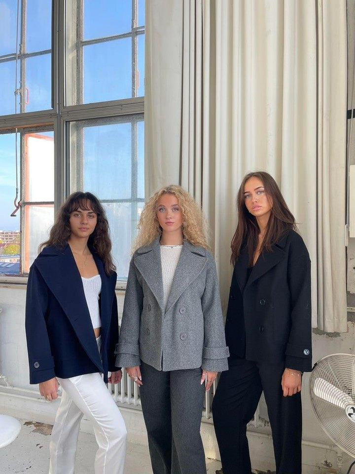 Drei Frauen in eleganten Blazern vor einem Fenster, modische Damenbekleidung, Herbstmode.