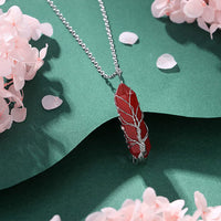 Rote Kristallkette mit silbernem Draht, auf grünem Hintergrund, umgeben von rosa Blüten.