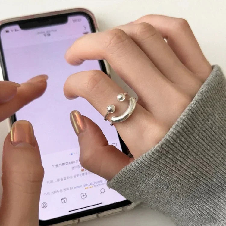 Silberner Smiley-Ring an Hand, Smartphone, grauer Pullover, modisches Accessoire, Damenmode.
