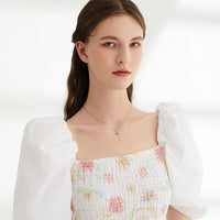 Frau in weißem, geblümtem Kleid mit Puffärmeln und Halskette, Porträtaufnahme.