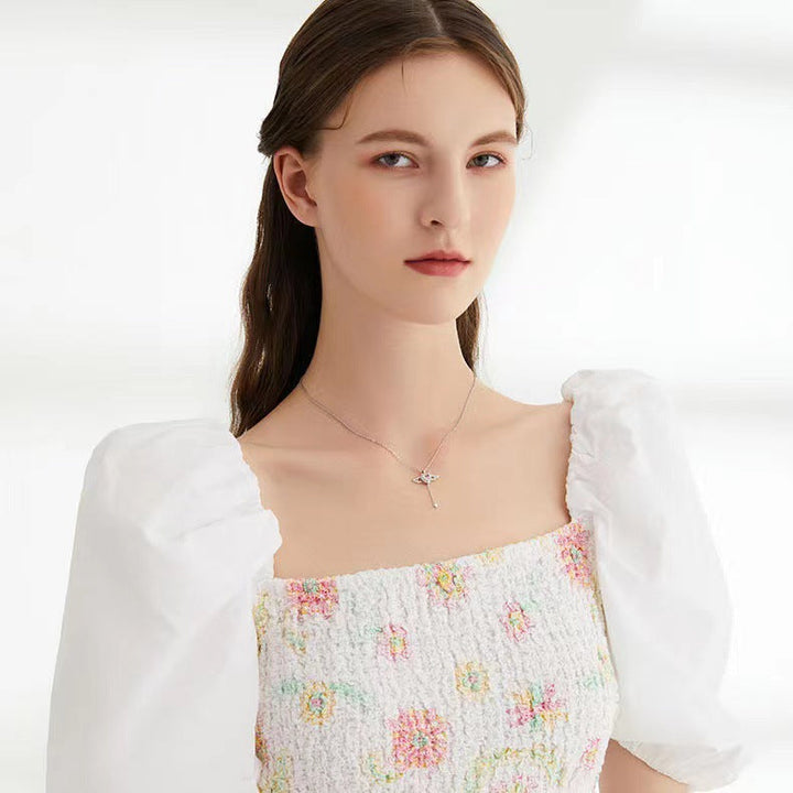 Frau in weißem, geblümtem Kleid mit Puffärmeln und Halskette, Porträtaufnahme.