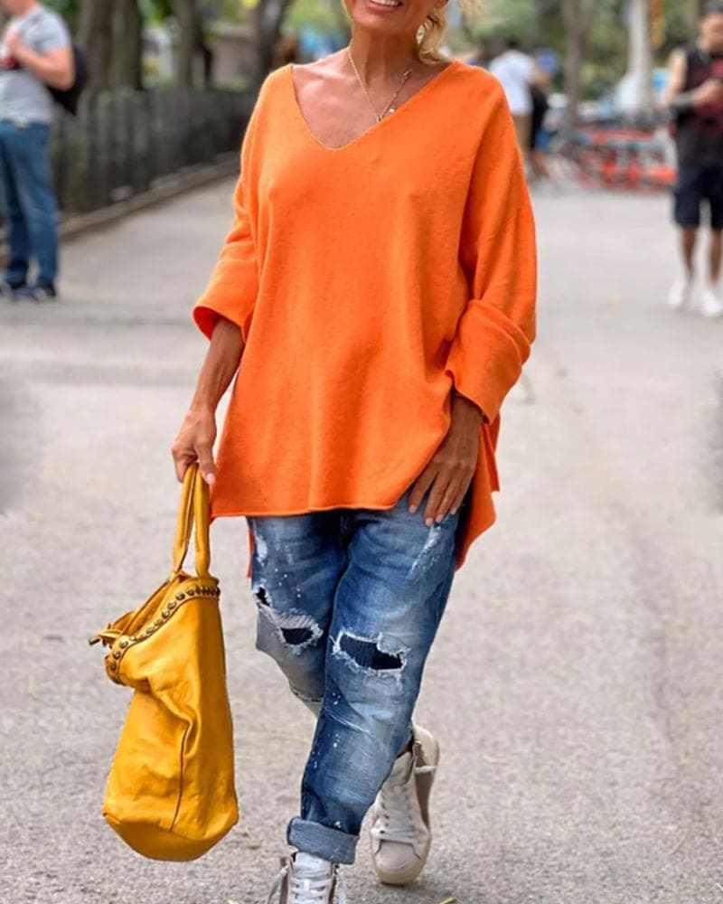 Frau in orangefarbenem Pullover, zerrissene Jeans, gelbe Tasche, lässiger Streetstyle-Look.