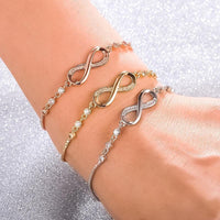 Drei Infinity-Armbänder in Gold, Silber und Roségold mit Strasssteinen auf Handgelenk.