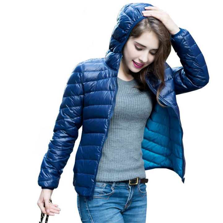 Frau in blauer Daunenjacke mit Kapuze, grauem Pullover und Jeans, modisch, outdoor.