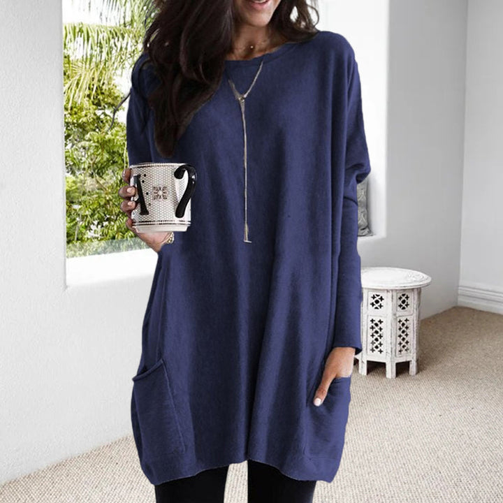 Frau in blauem Oversize-Pullover mit Tasse, lässige Mode, Wohnzimmer, Tageslicht.