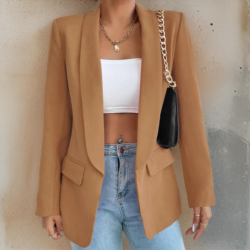 Frau in braunem Blazer, weißem Top, blauer Jeans, schwarze Tasche mit Kettengurt.