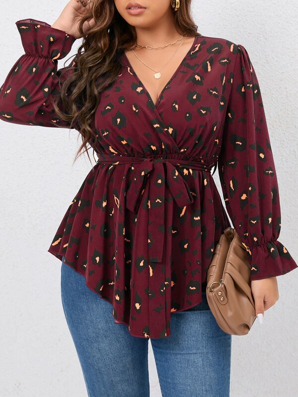 Frau in roter Leopardenbluse mit V-Ausschnitt und blauer Jeans, hält braune Handtasche.