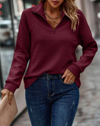 Frau in bordeauxrotem Pullover mit Reißverschluss, blaue Jeans, Stadtstraße, modisch, Herbstlook.