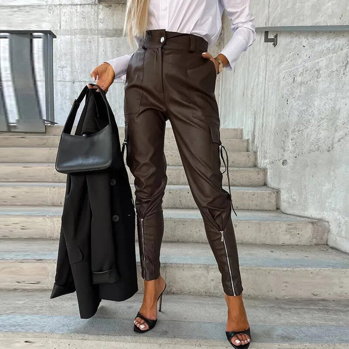 Frau in brauner Lederhose, weißer Bluse, schwarze Tasche, High Heels, moderne Mode.