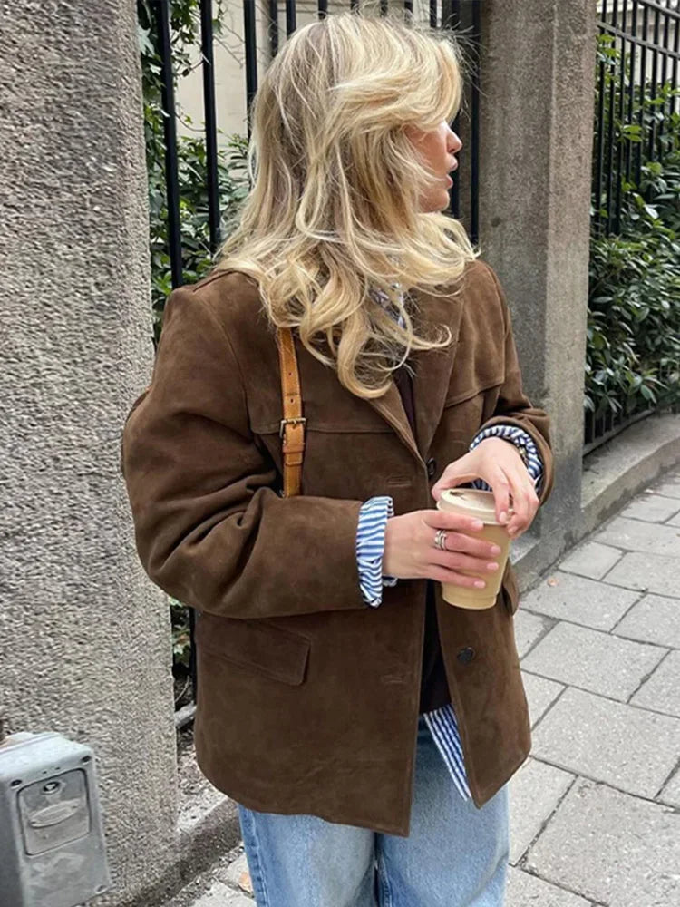 Frau in brauner Wildlederjacke mit Kaffeebecher, blonde Haare, lässiger Streetstyle-Look.