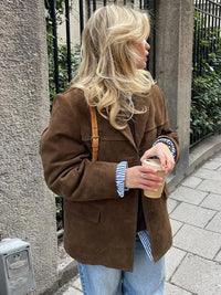 Frau in brauner Wildlederjacke mit Kaffeebecher, blonde Haare, lässiger Streetstyle-Look.