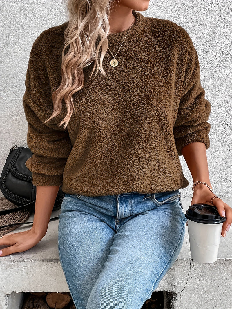 Frau in braunem Fleece-Pullover, blaue Jeans, hält Kaffeebecher, modisch, lässiger Look.