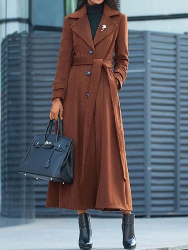 Frau in braunem Trenchcoat mit schwarzer Handtasche und Stiefeln, elegantes Herbstoutfit.