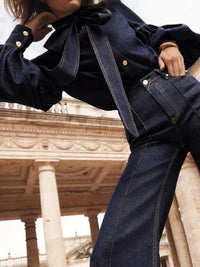 Frau in dunkelblauer Jeansbluse und Hose vor historischer Architektur, Mode, Denim, elegant.