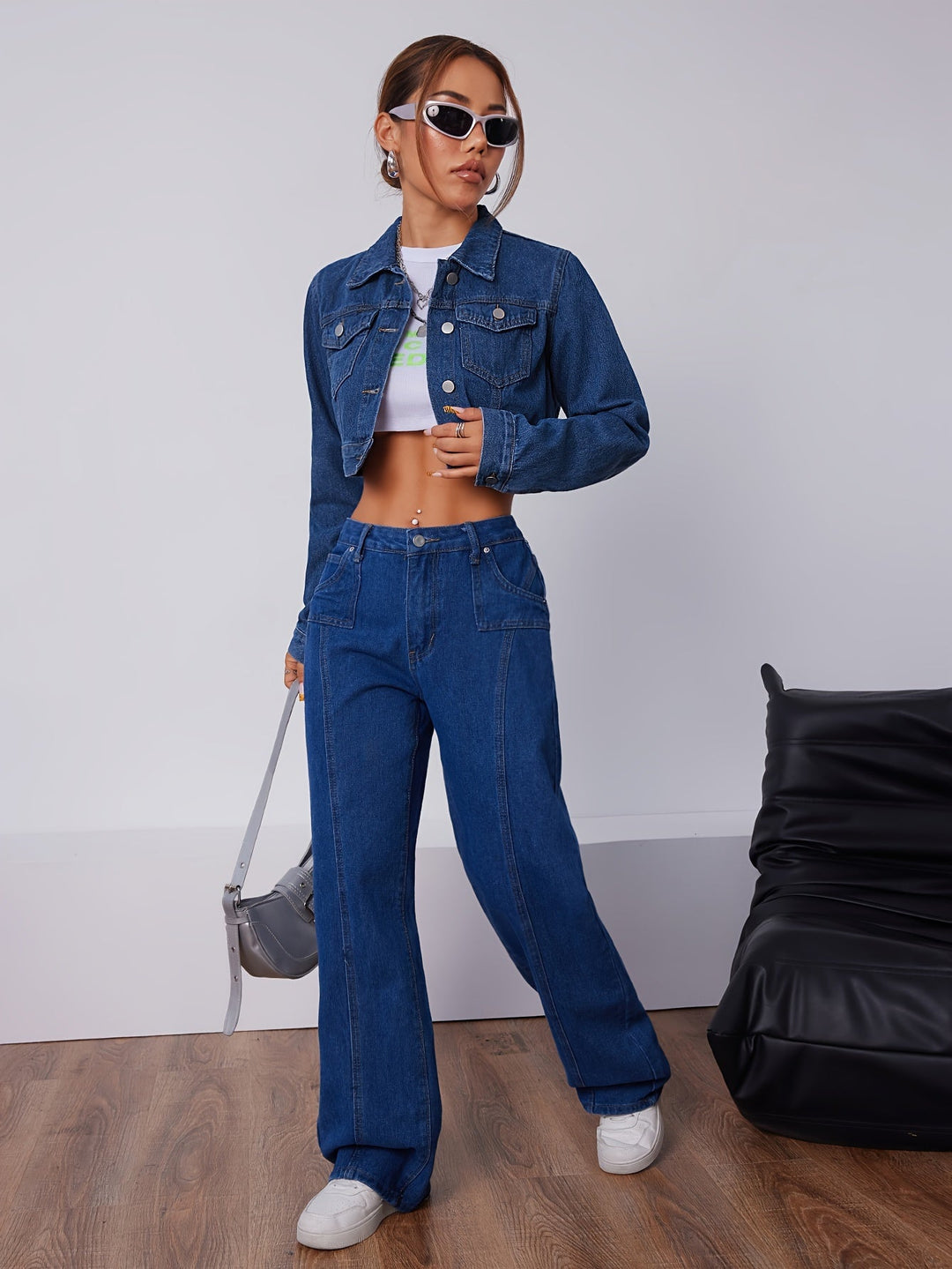 Frau in blauer Jeansjacke und Jeanshose, weißes Crop-Top, Sonnenbrille, modisch, lässig.